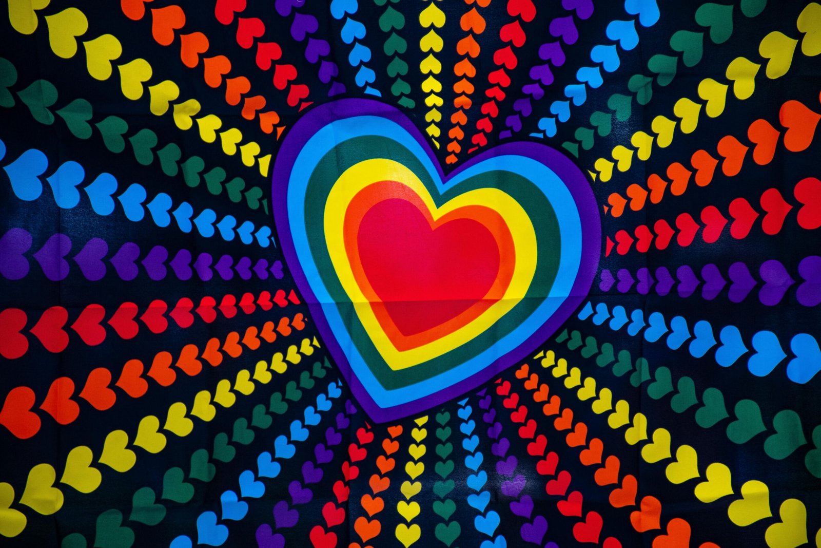 Colorful heart design with rainbow gradients and radiant pattern of small hearts on black background.